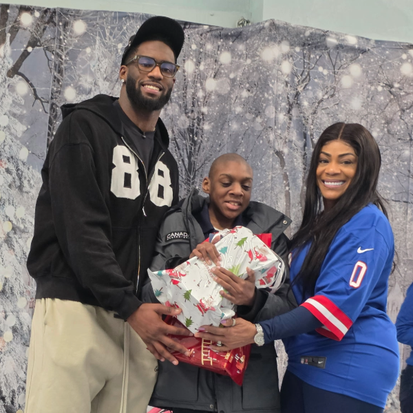 Smiling group of three holding wrapped presents in a snowy forest.