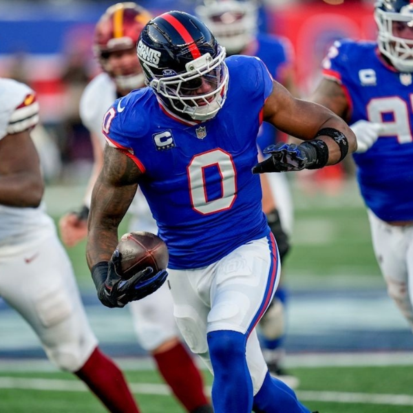 Football player Brian Burns in a blue jersey running with the ball, fiercely determined. Teammates and opponents in action, conveying intensity and focus of the game.