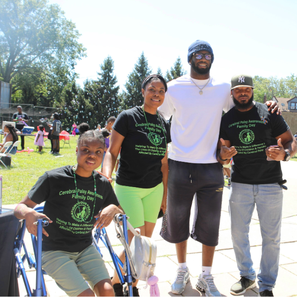 Four people at an outdoor event; two men and two women, one seated with a walker.