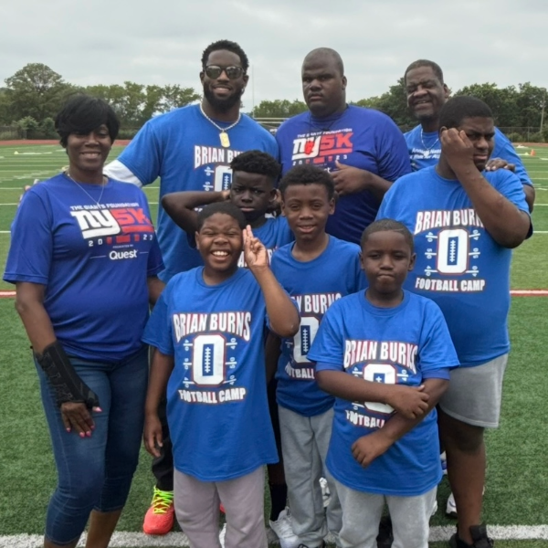 A group of nine people on an athletic field, wearing themed T-shirts related to a football camp and a 5K event.