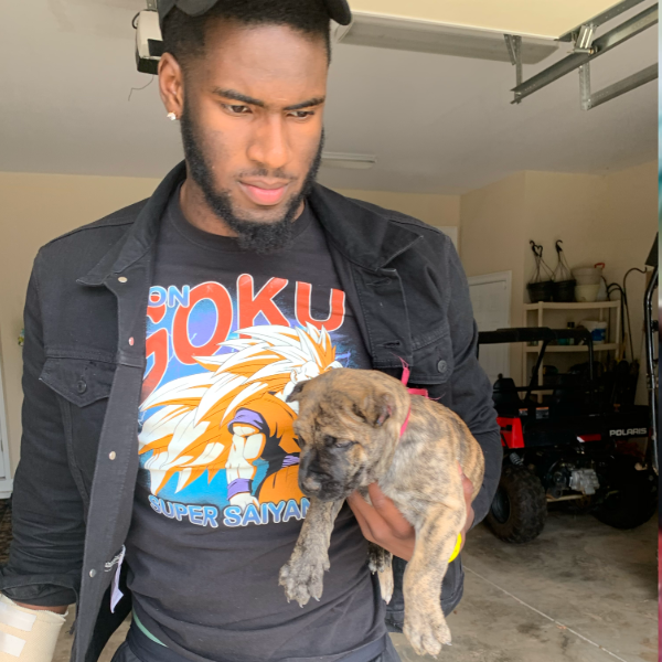 Brian Burns in a garage holding a brindle puppy, wearing a graphic T-shirt with a character and text